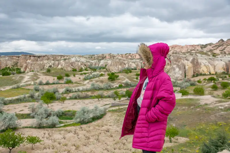 Woman in pink coat standing amid Cappadocia's unique scenic rock formations.